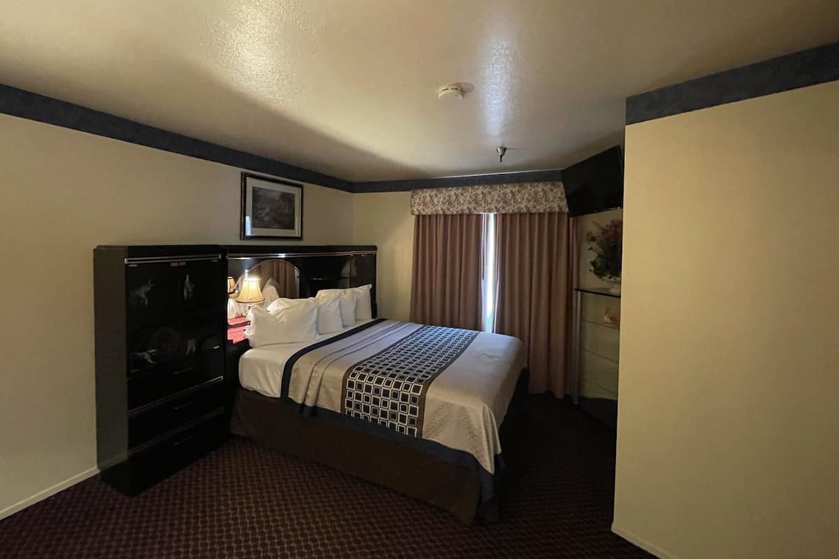 A hotel room with a bed, a nightstand, a lamp, a dresser, and a window with curtains.