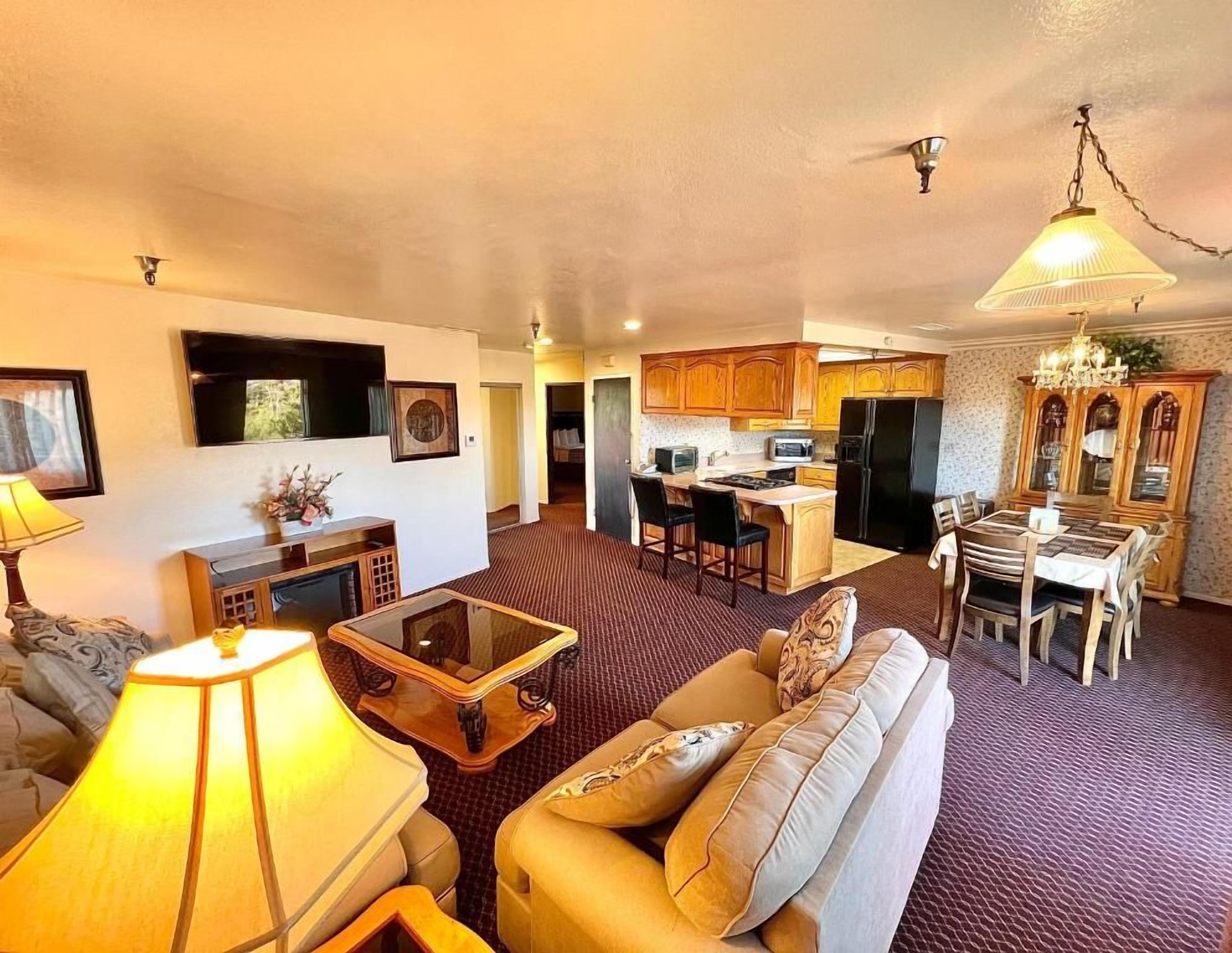 A living room with a sofa, coffee table, and lamp. There is a kitchen area with a refrigerator, microwave, and dining table.