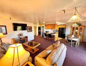 Sala de estar con sofá, mesa de centro y lámpara. Zona de cocina con refrigerador, microondas y mesa de comedor.
