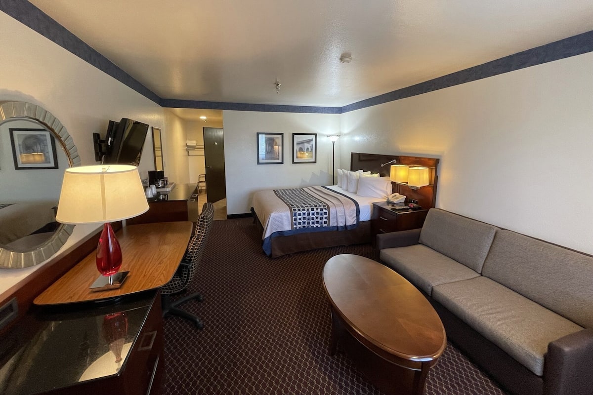 A hotel room with a bed, a sofa, a desk with a lamp, a chair, and a small table.