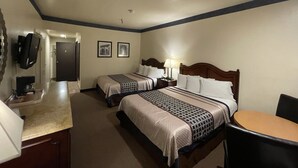 A hotel room with two beds, a desk, a chair, a TV, and a door.