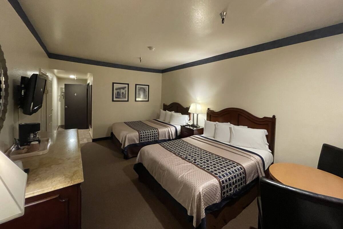 A hotel room with two beds, a desk, a chair, a TV, and a door.