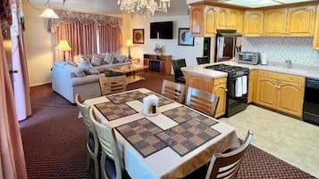A dining area with a table set for four, a chandelier, and a kitchen in the background.
