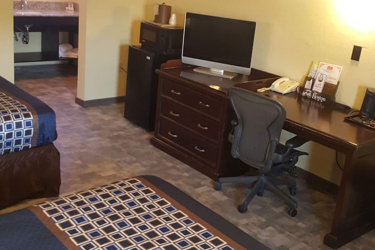 A hotel room with a desk, computer, telephone, and a kitchenette area.