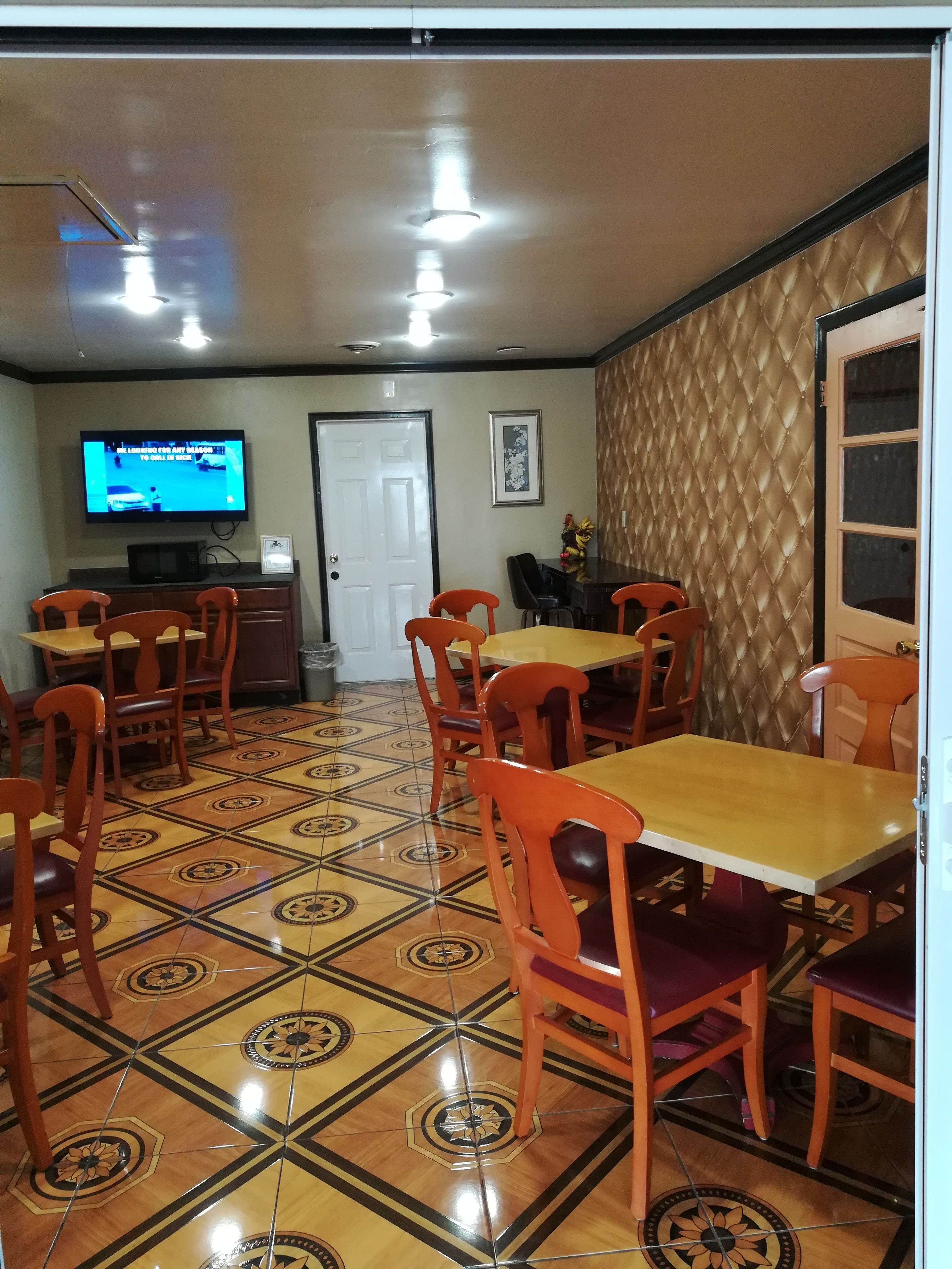 A dining area with patterned tile flooring, orange chairs, and a television mounted on the wall.