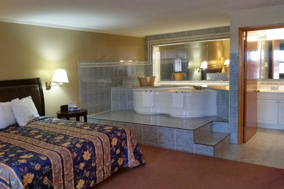 Habitación de hotel con cama, una bañera grande, un espejo y un mueble de baño.
