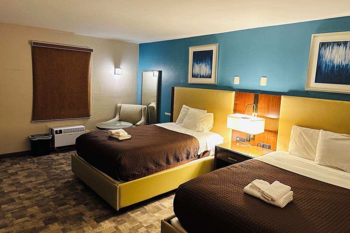 A hotel room with two beds, a chair, a desk, and a mirror.