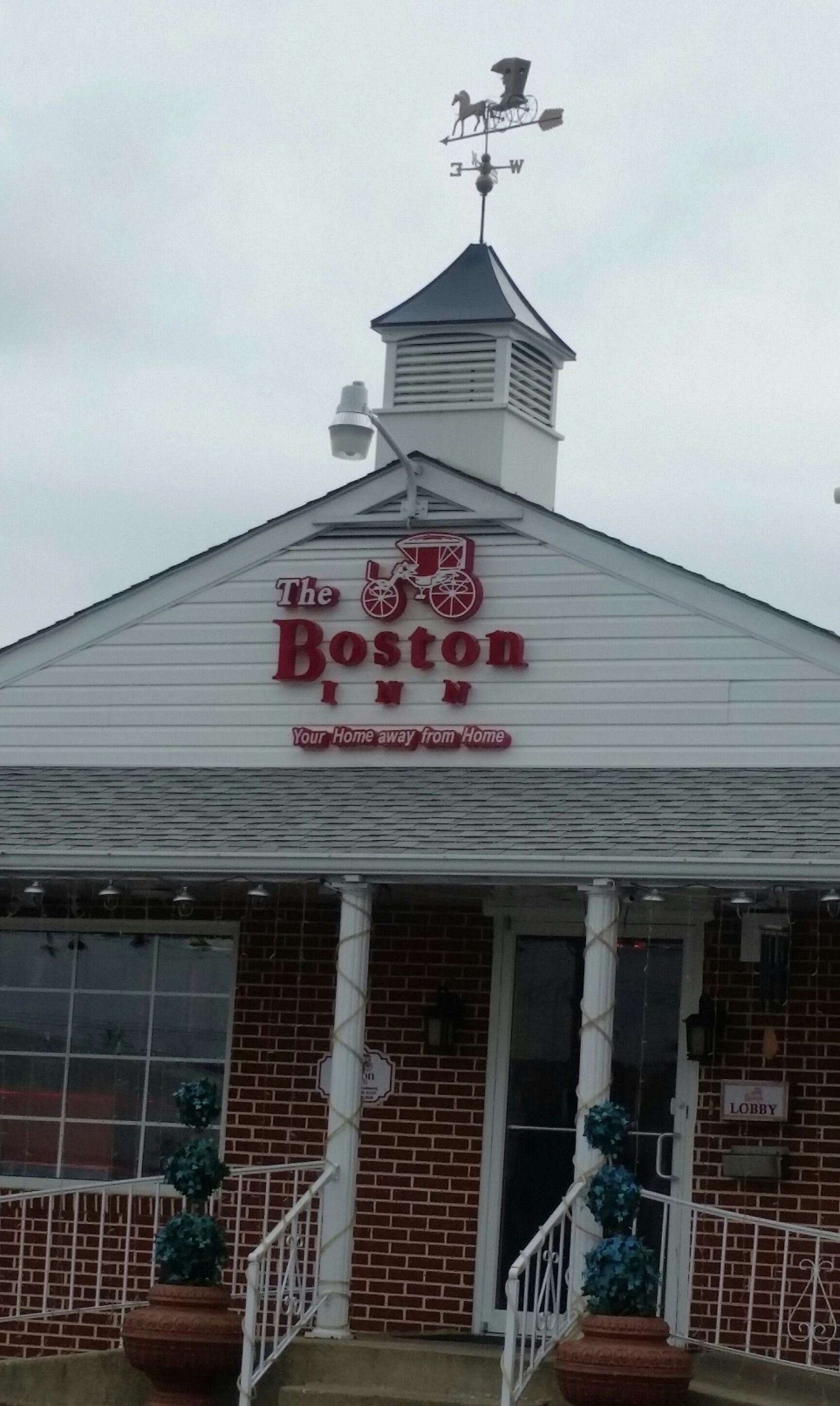 The Boston Inn with a weather vane, a sign reading "Your Home away from Home," and brick exterior walls.
