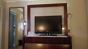 A hotel room with a flat-screen TV mounted on a wooden cabinet, a door leading to another room, and a wall-mounted light fixture.
