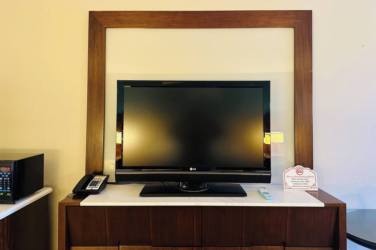 A television on a wooden stand with a remote control and a phone beside it.