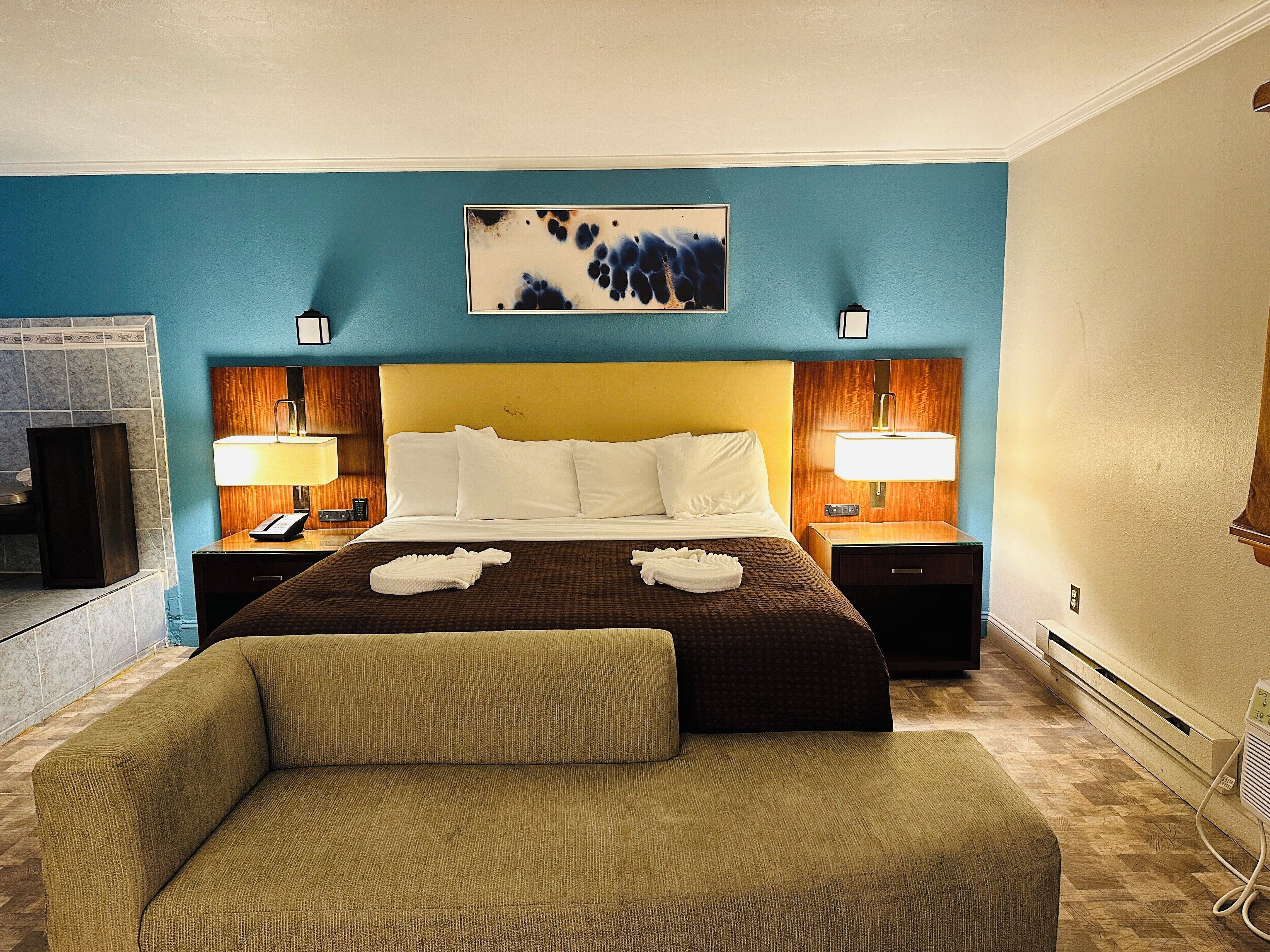 A hotel room with a large bed, two bedside tables with lamps, a painting above the bed, and a small seating area.