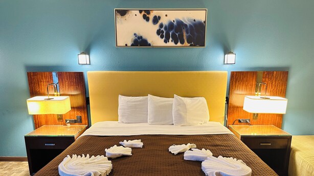 A hotel room with a large bed, two bedside lamps, a painting on the wall, and towels arranged on the bed.