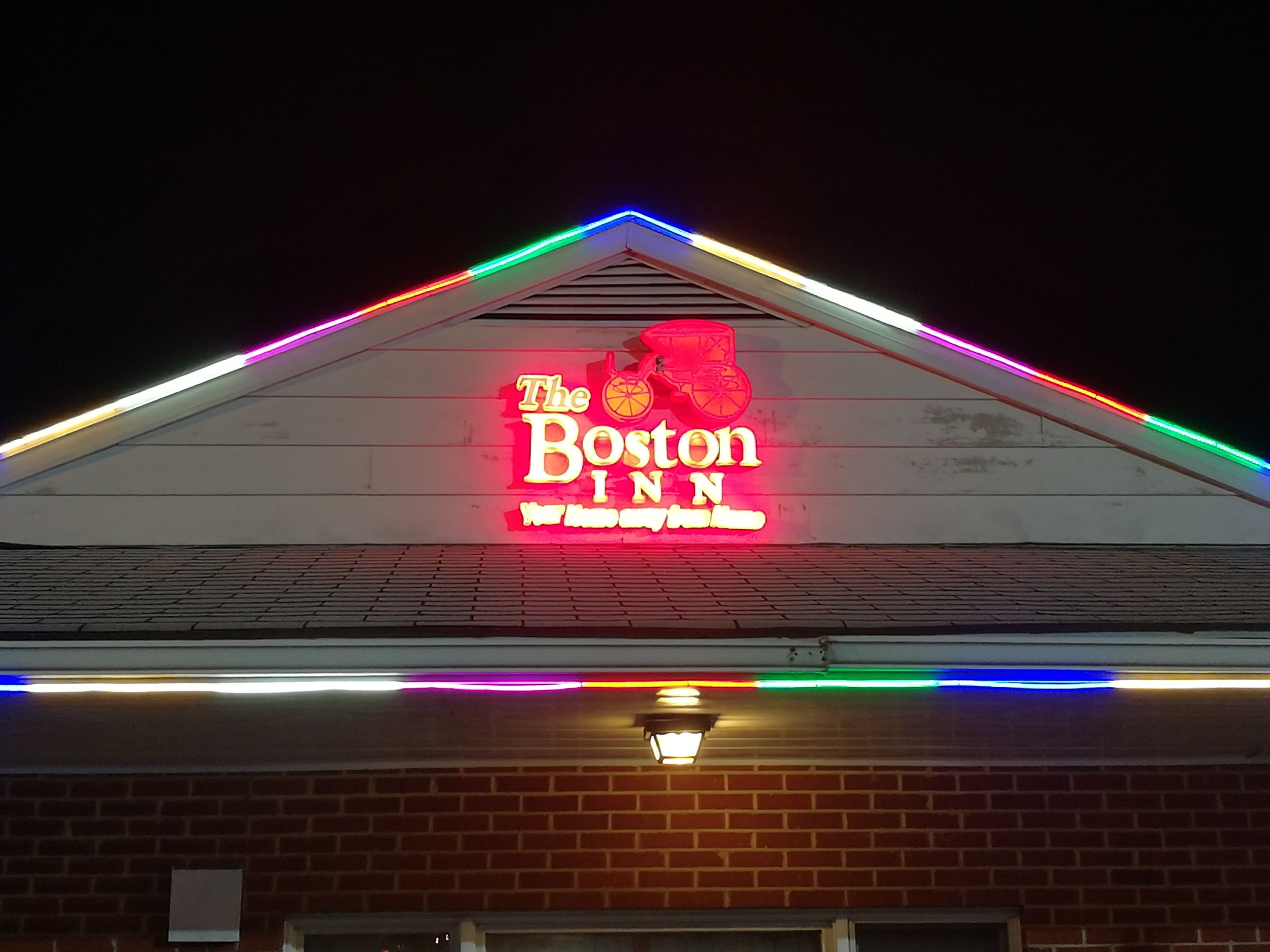 A building with a neon sign for 'The Boston Inn' and colorful LED lights along the roofline.