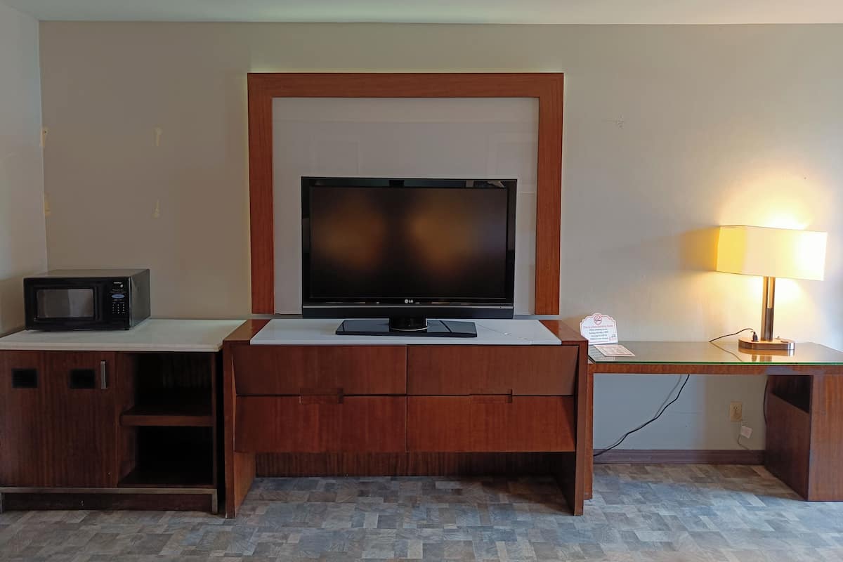 A hotel room with a wooden desk, a flat-screen TV, a microwave, and a desk lamp.