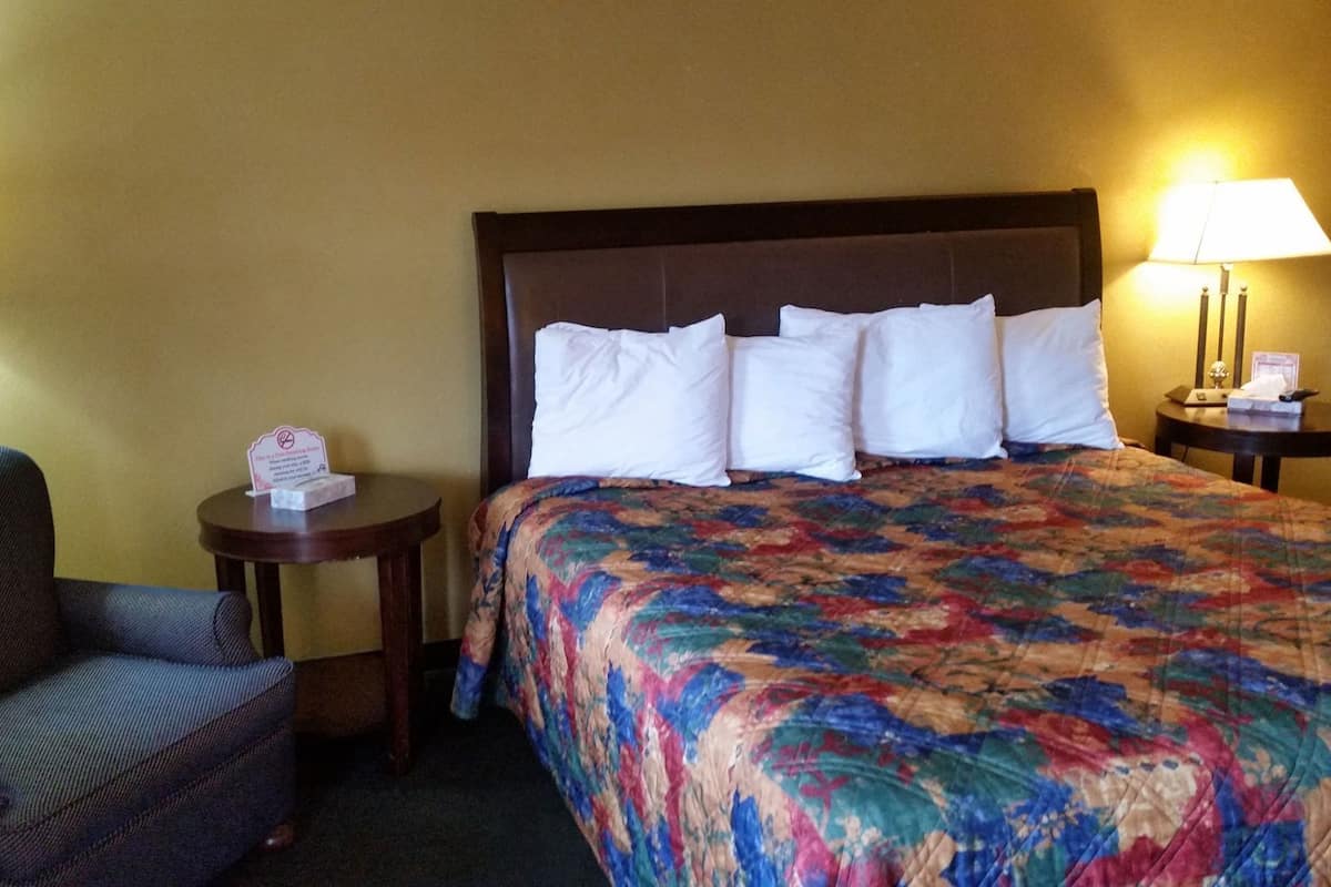 A hotel room with a bed, a chair, two nightstands, and lamps.