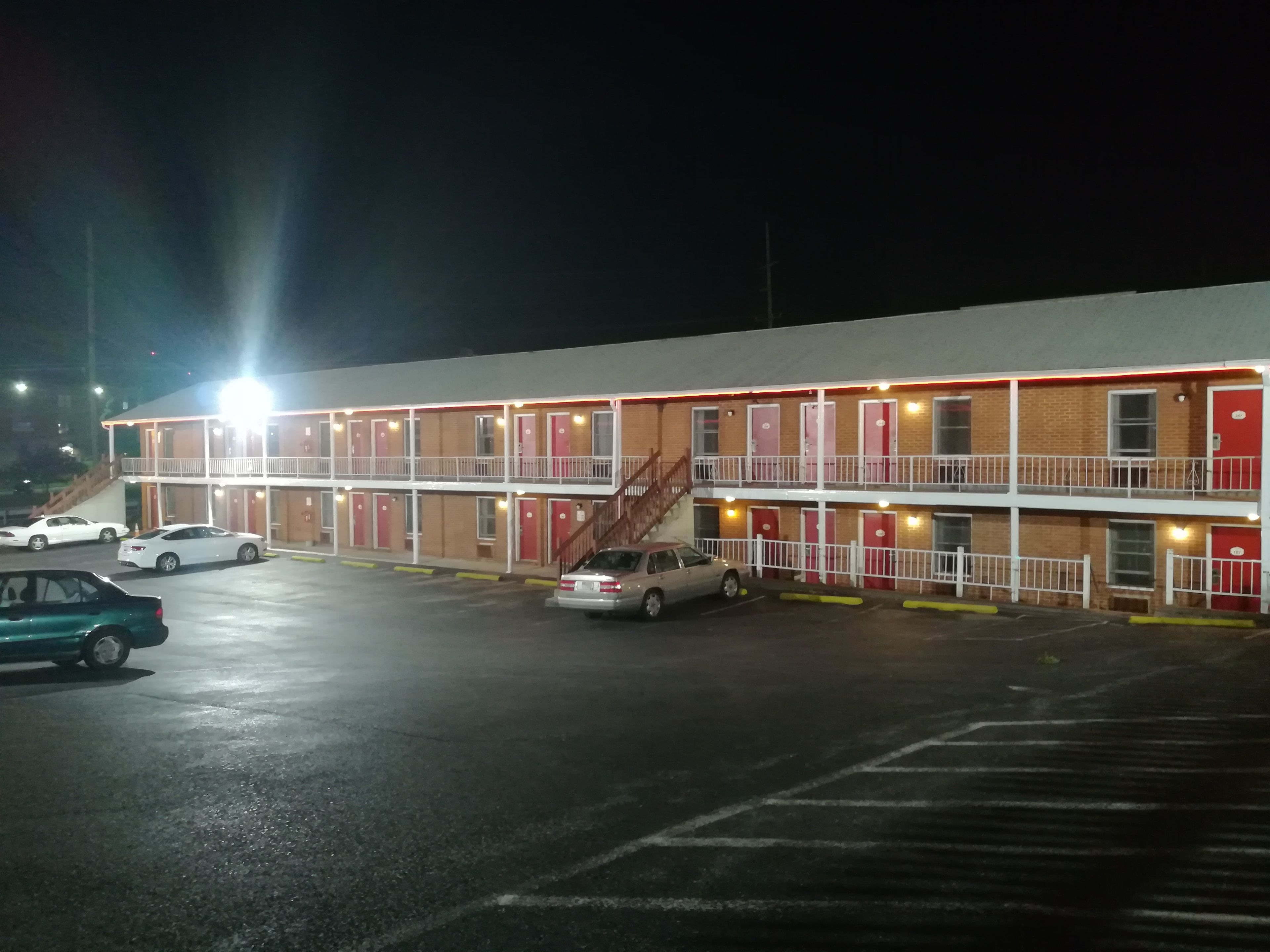 A motel with a two-story structure, multiple rooms, and a parking lot with several cars.