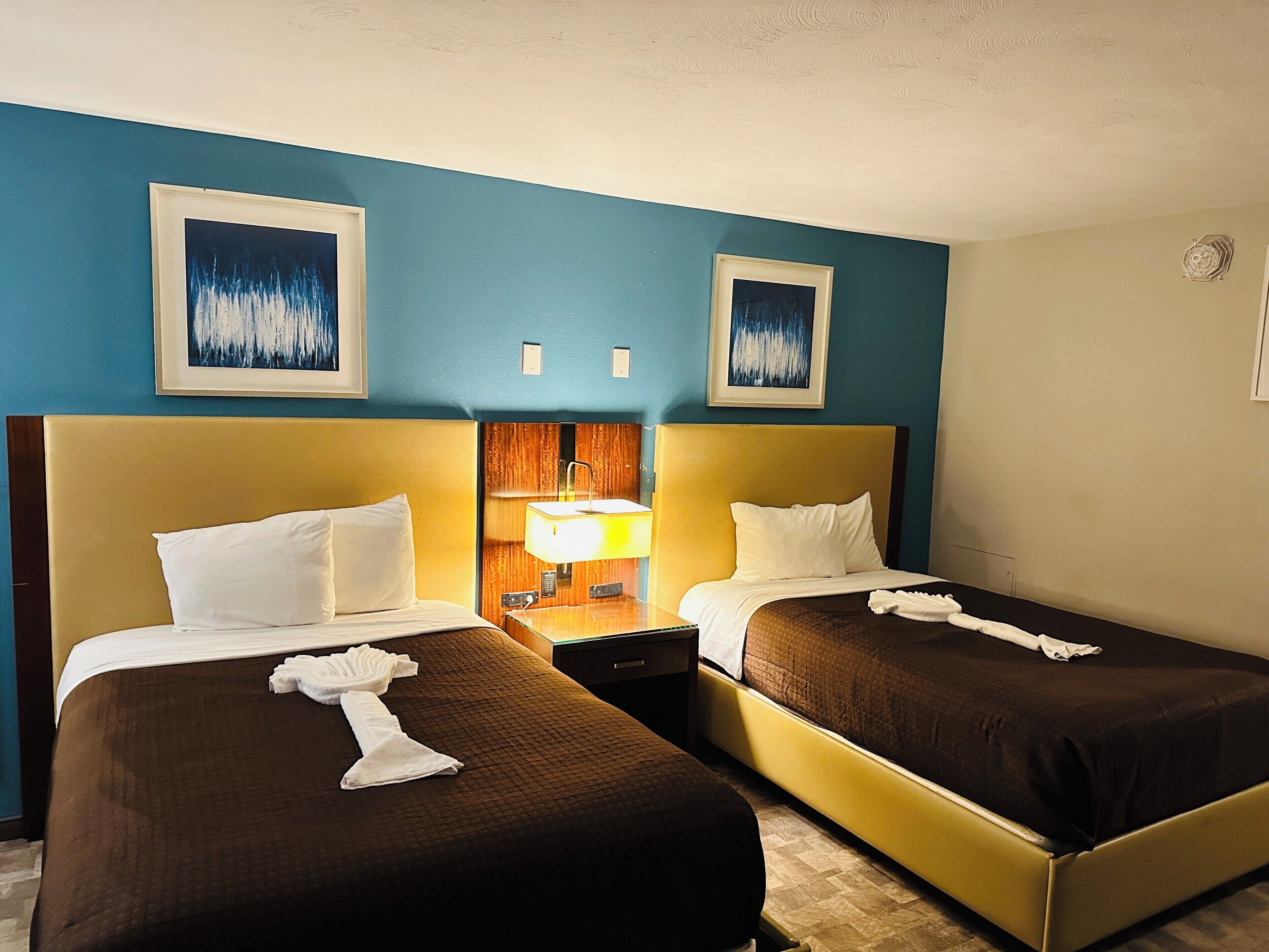 Ein Hotelzimmer mit zwei Betten, einem Nachttisch mit Lampe und Bildern an der Wand.