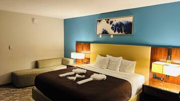 A hotel room with a large bed, a bedside table with a lamp, a small sofa, and a painting on the wall.