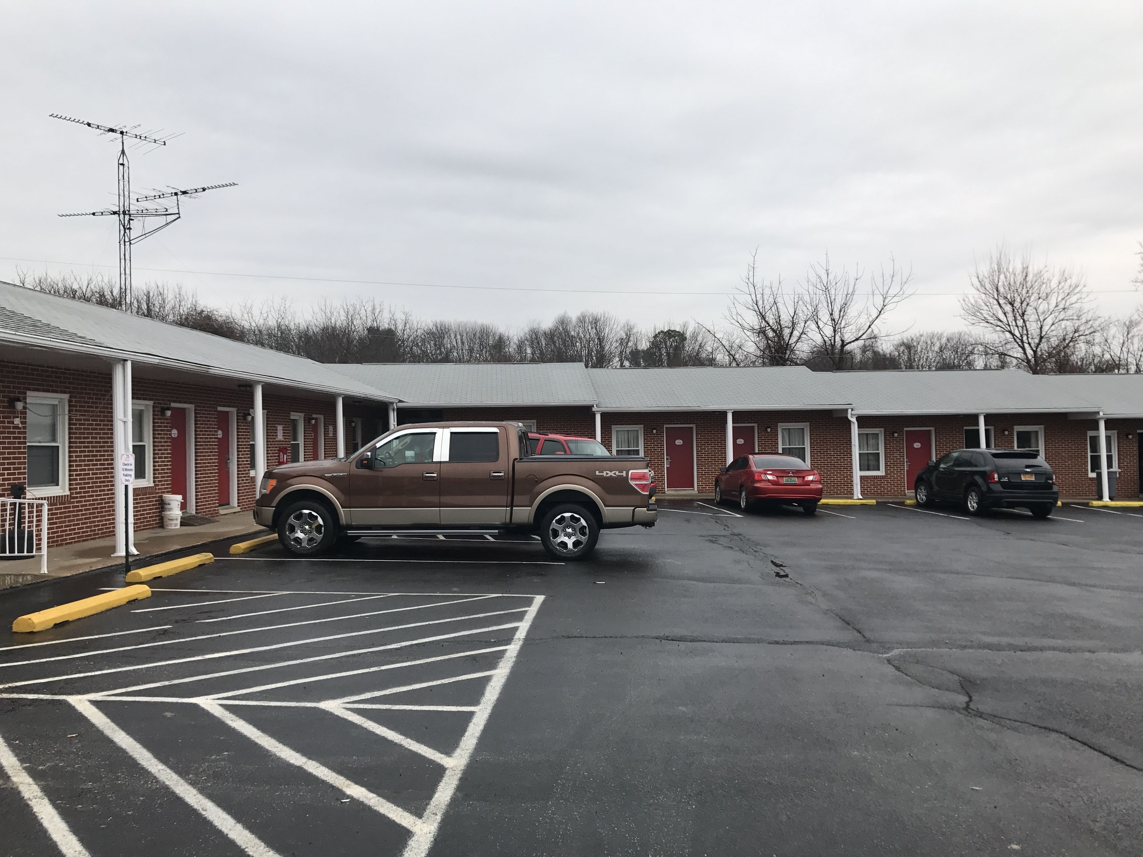 A motel with a parking lot, a brown pickup truck, and a red car parked in front.