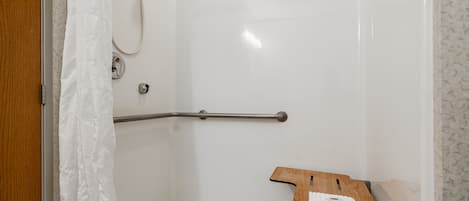 A shower area with a wooden bench, a grab bar, and a towel on the bench.