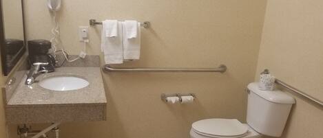 Ein kleines Badezimmer mit Waschbecken, Toilette, Handtrockner und Haltegriff.
