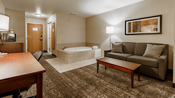 A hotel room with a wooden desk, a sofa, a coffee table, a large painting on the wall, a bathtub, and a lamp. - Cobblestone Suites - Ripon (Ripon)