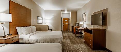 A hotel room with two beds, a desk, a TV, and a coffee machine.