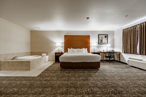 A hotel room with a large bed, a separate bathroom with a bathtub, a desk with a chair, and a large window with curtains.