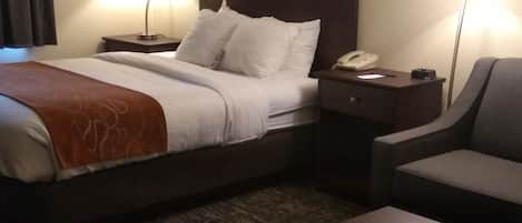 Quarto de hotel com uma cama, mesa de cabeceira com abajur, uma cadeira e uma mesinha.