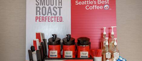 A coffee station with labeled coffee dispensers, a bowl of snacks, and a sign stating "Seattle's Best Coffee."