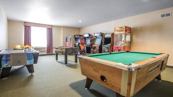 A pool table, a foosball table, and several arcade machines in a room with beige walls and a carpeted floor.