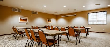 A conference room with multiple tables and chairs, recessed ceiling lights, and large windows.