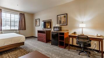 A hotel room with a bed, desk, chair, TV, microwave, and a lamp.