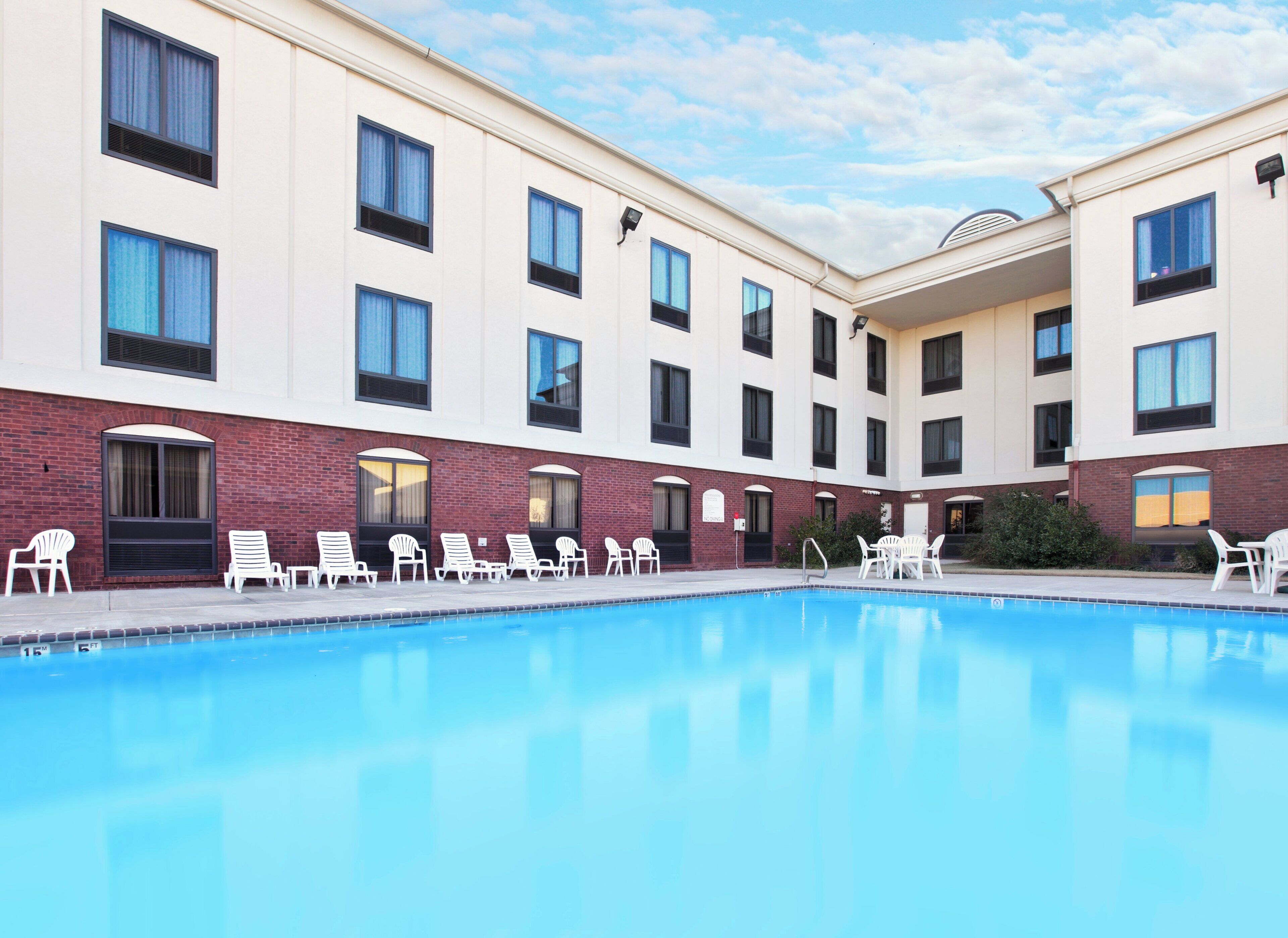Ein Hotel mit Schwimmbad, mehreren Fenstern und weißen Stühlen, die um das Becken angeordnet sind.
