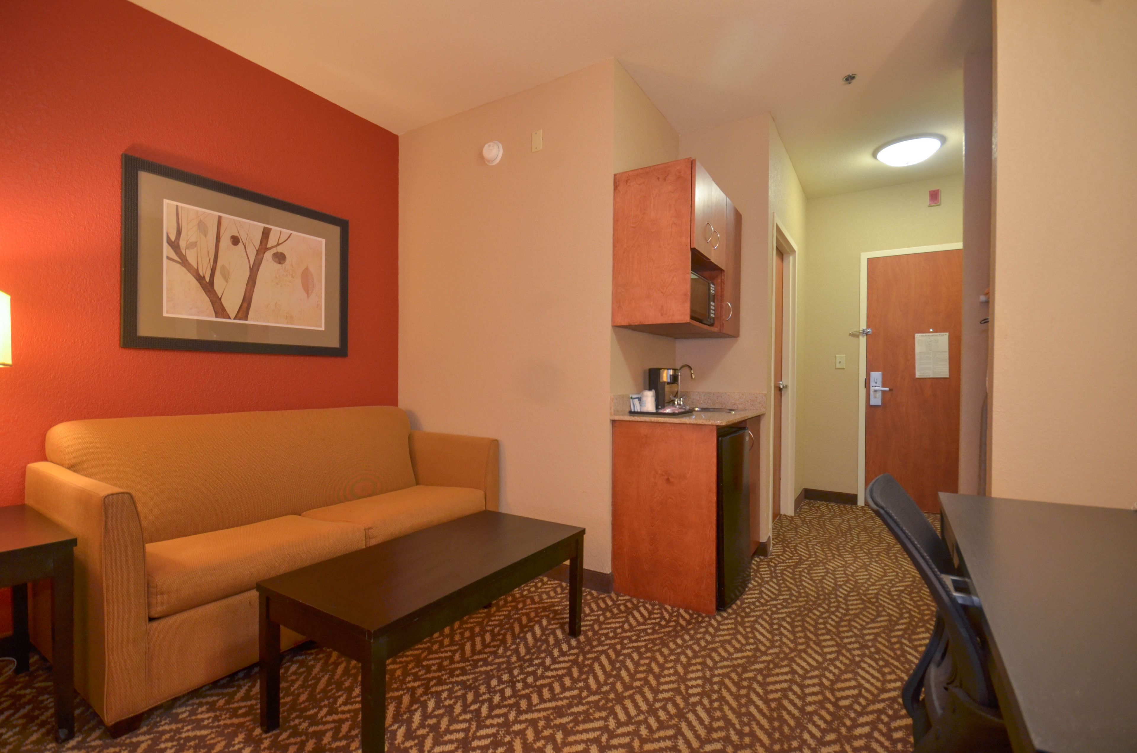 Une chambre d’hôtel avec un canapé, une petite table, un coin cuisine et un tableau encadré au mur.