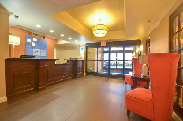 A hotel reception area with a wooden reception desk, a blue sign with 'Express' branding, a red chair, and a chandelier. - Holiday Inn Express Hotel & Suites Pine Bluff / Pines Mall by IHG (Pine Bluff)