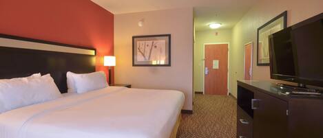 A hotel room with a large bed, a television, a desk, and a door leading to another room.