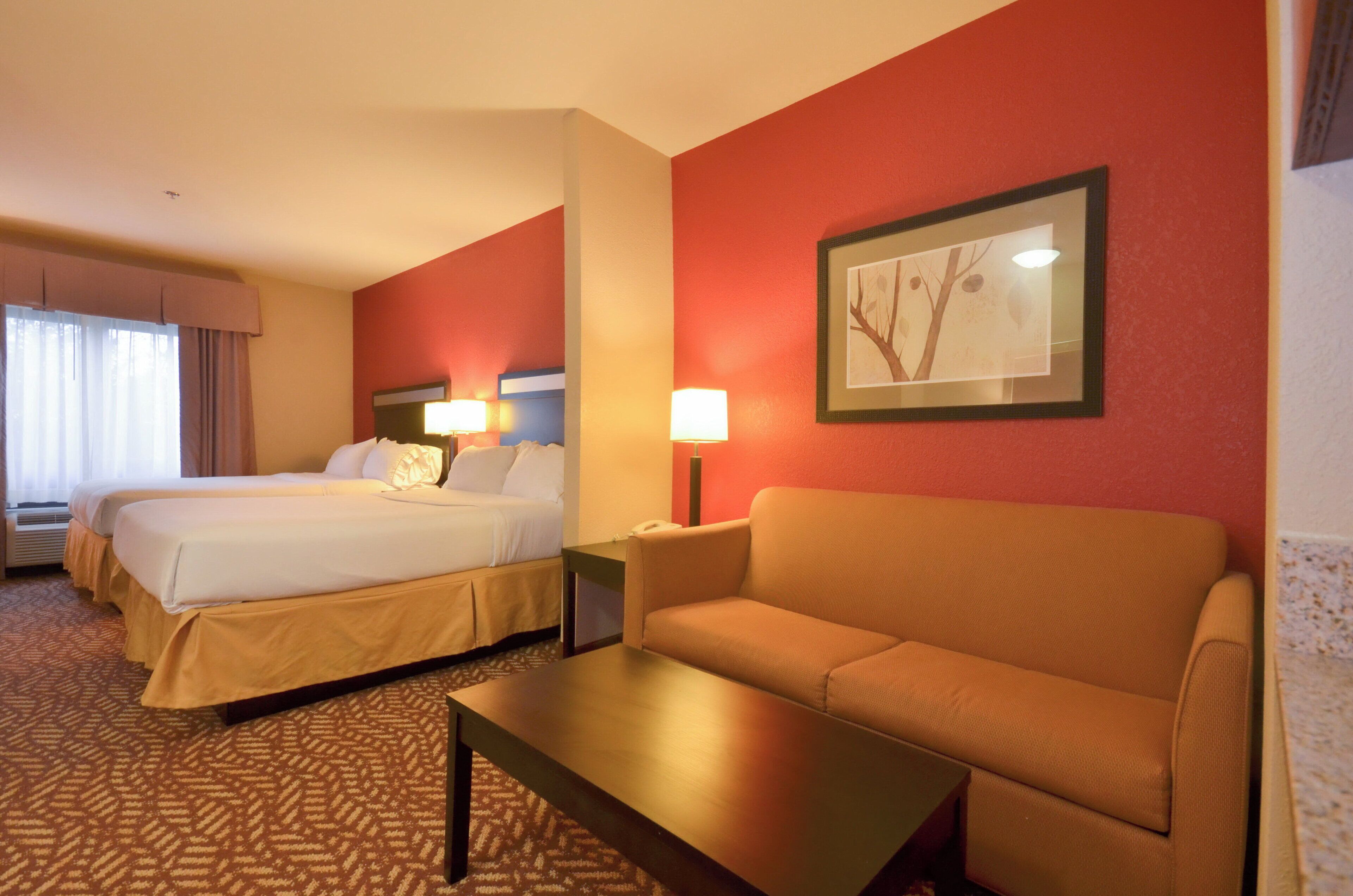 A hotel room with two beds, a sofa, a table, and a framed picture on the wall.