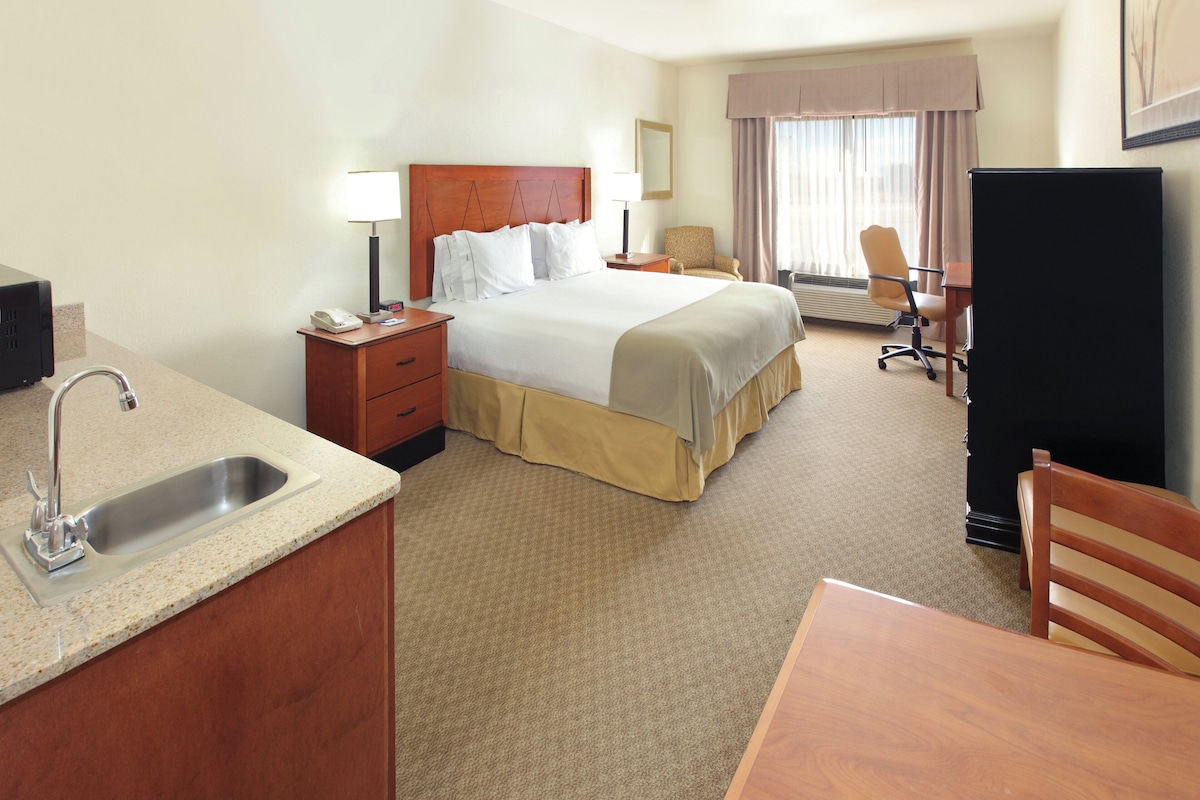 A hotel room with a bed, a desk, a chair, a desk lamp, a telephone, and a sink.
