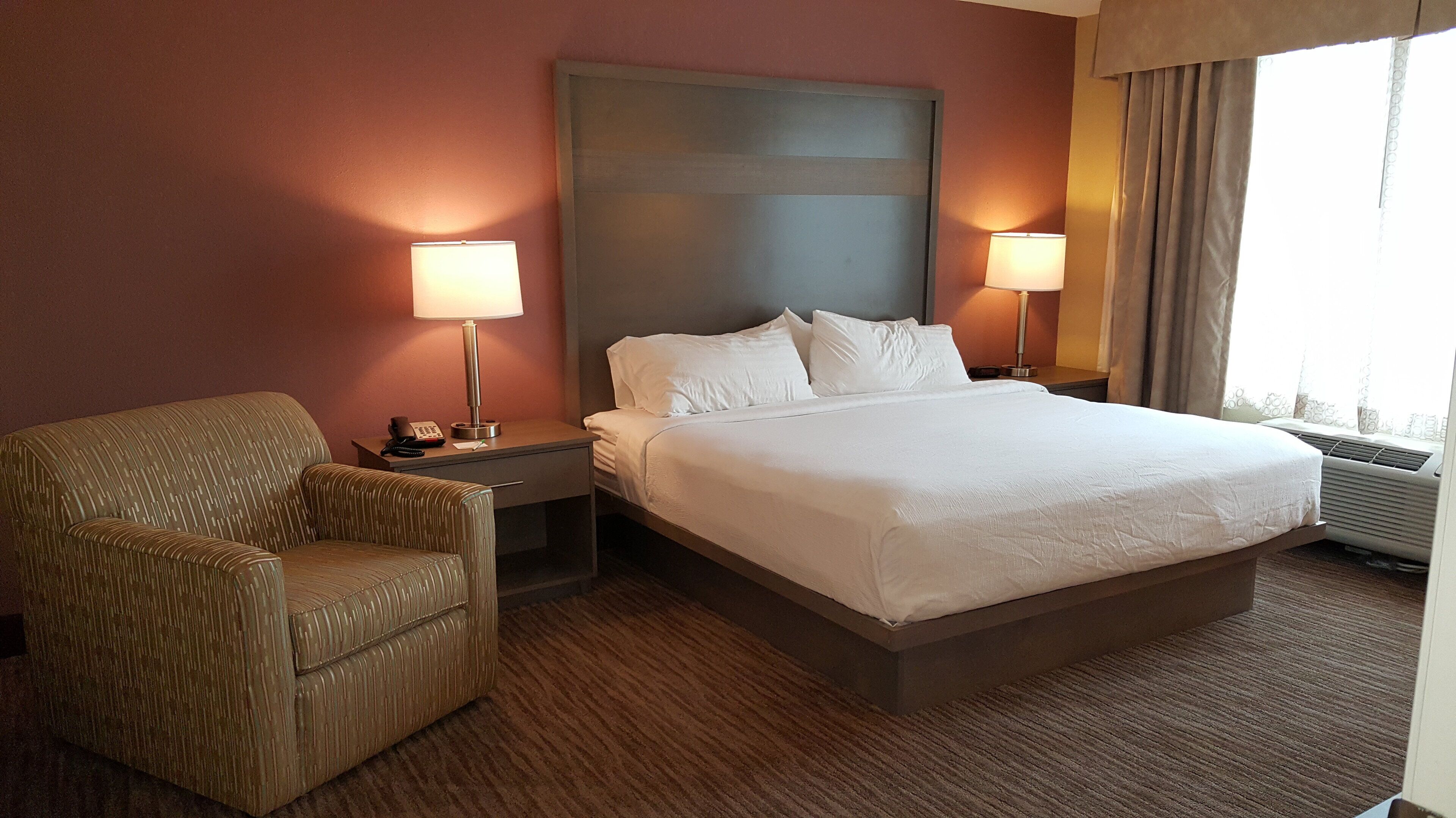 A hotel room with a large bed, two bedside lamps, a chair, and a nightstand with a phone.