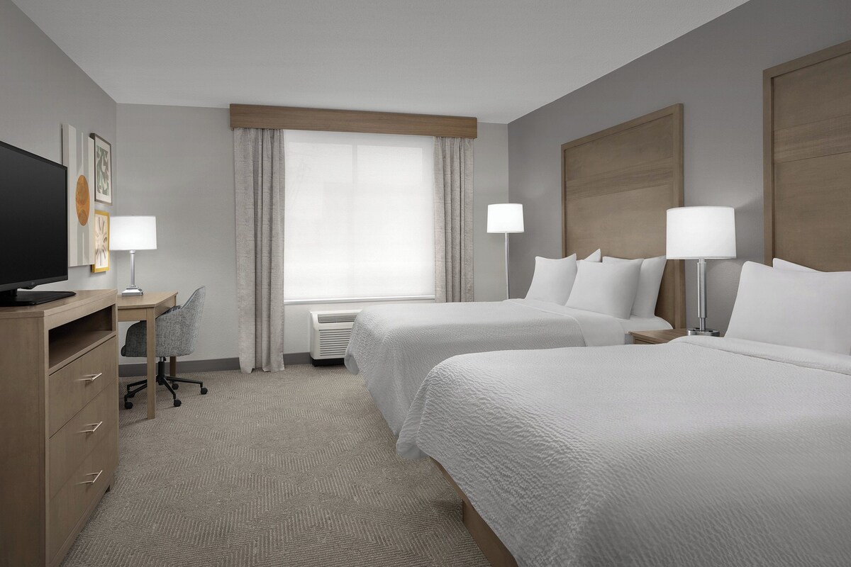 Een hotelkamer met twee bedden, een bureau, een stoel, een televisie en een raam met gordijnen.
