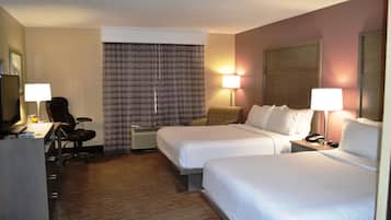 A hotel room with two beds, a desk with a chair, a desk lamp, a telephone, and a wall-mounted TV.