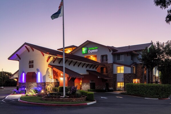 Ein Holiday Inn Express Hotel mit moderner Architektur, das einen markanten Eingang, angelegte Gärten und eine Fahnenstange zeigt.