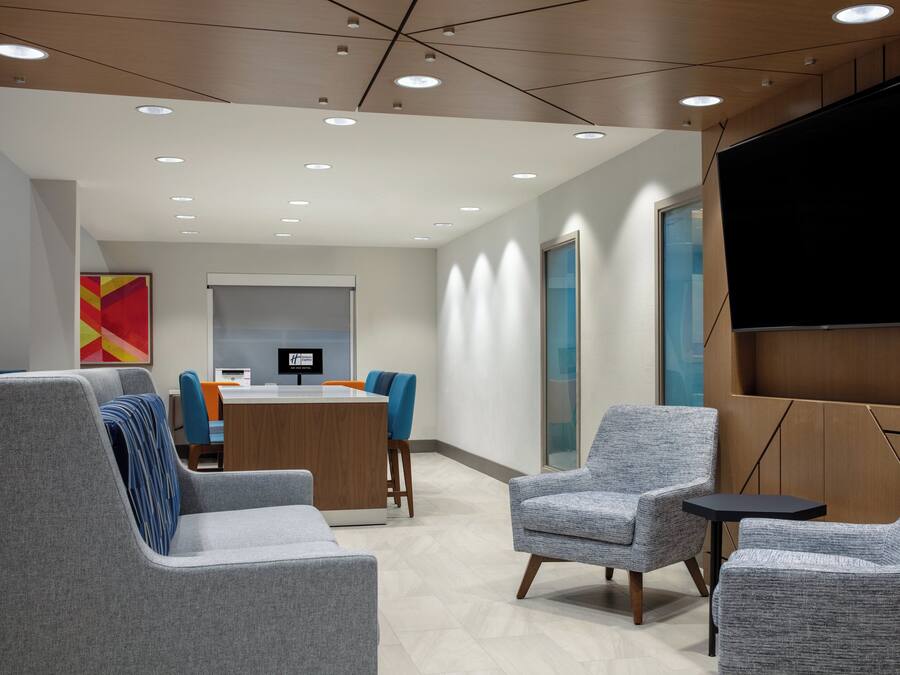 A modern waiting area with grey upholstered chairs, a reception desk, and a large flat-screen TV mounted on the wall.