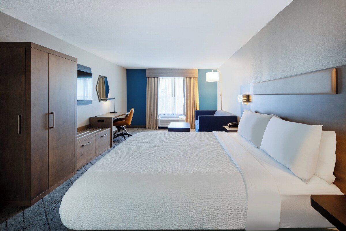 Ein Hotelzimmer mit einem großen Bett, einem Schreibtisch, einem Stuhl, einem Kleiderschrank und einem fenster mit Vorhängen.