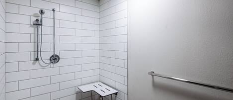 Un área de ducha pequeña, con azulejos blancos y un cabezal de ducha de mano, además de un accesorio de ducha portátil.