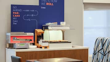 A breakfast station with a flat-top griddle, a sign indicating fresh pancakes in a minute, and a menu board with breakfast options.