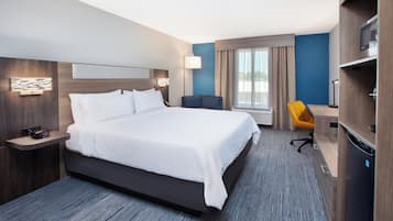 A modern hotel room with a large bed, a desk, a chair, a TV, and a minibar.