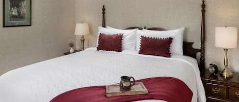 A neatly made bed with a white quilt, two red pillows, and a tray with a mug on the bed.