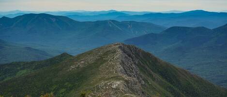 A mountain landscape with a prominent peak, surrounded by forested areas and distant mountain ranges.